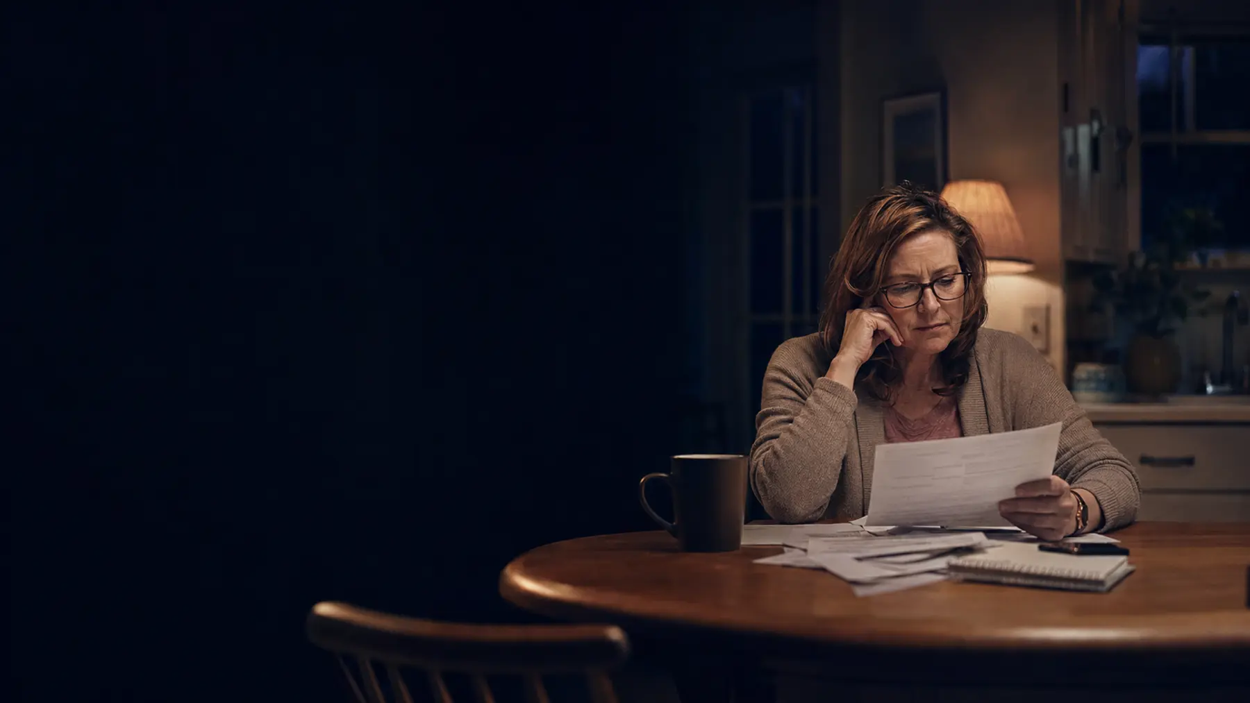 A woman reviewing paperwork late at night at her kitchen table